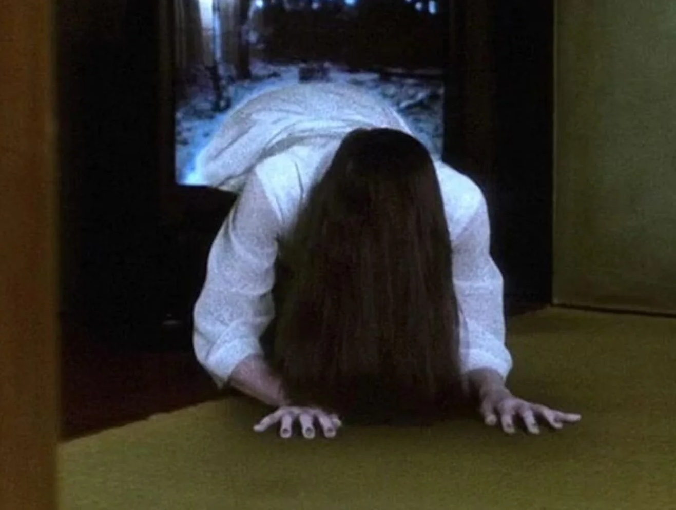 Cadru din filmul Ringu: Sadako, în rochie albă și cu părul lung peste față, se târăște afară din ecranul unui televizor