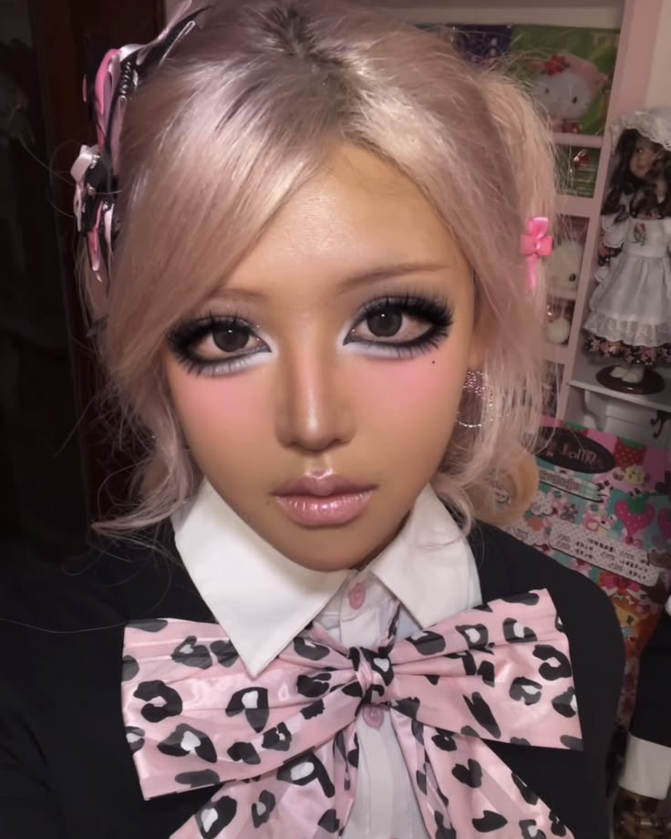 Machiaj gyaru: ten bronzat, ochi conturați cu negru și alb, gene false voluminoase, blush roz, păr blond cu panglici roz