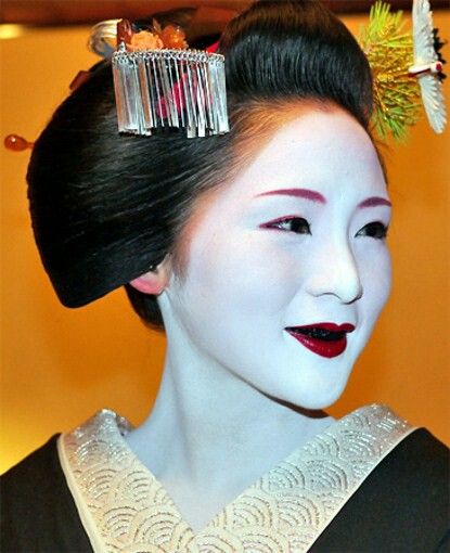 Femeie în machiaj tradițional japonez: ten alb, sprâncene și buze roșii, păr strâns cu agrafe ornamentale